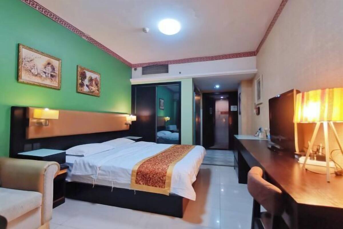 Une chambre d’hôtel avec un lit, des tables de chevet, un bureau et une chaise. Deux tableaux encadrés sont accrochés au mur.