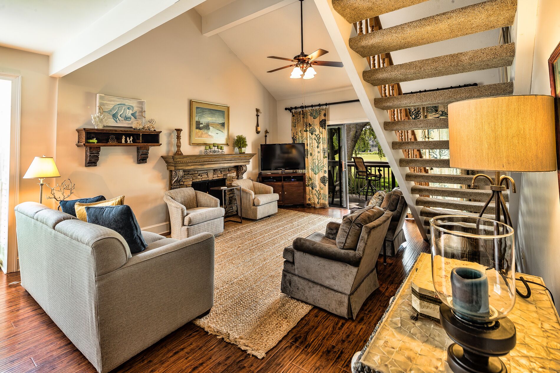 A spacious living room with a fireplace, comfortable seating, a television, and a staircase with a unique design.