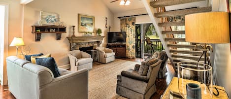 A spacious living room with a fireplace, comfortable seating, a television, and a staircase with a unique design.