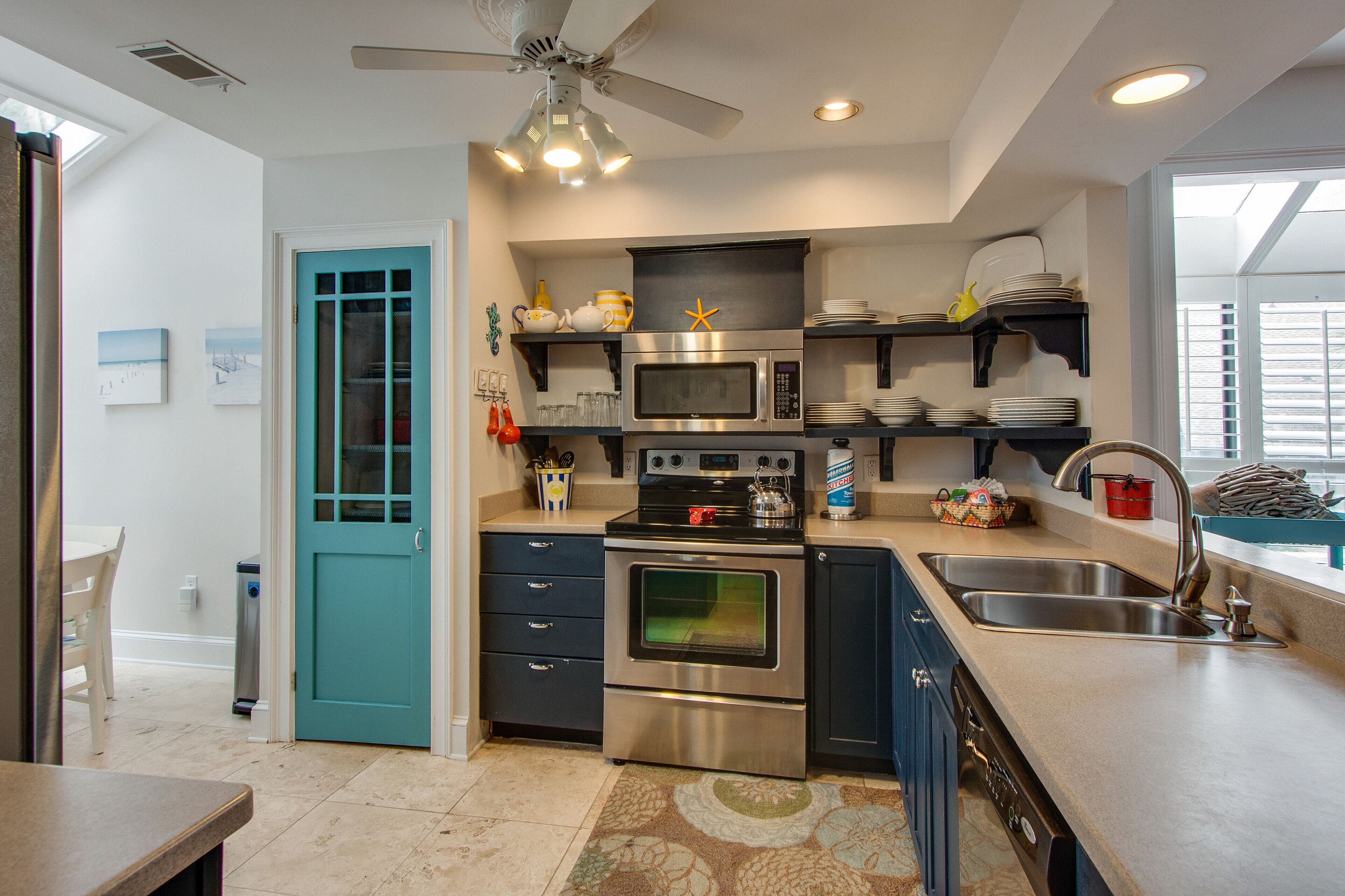 A modern kitchen with a teal door, stainless steel appliances, and a ceiling fan.