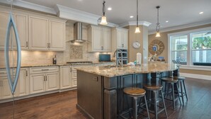 Un'ampia cucina con mobili bianchi, una grande isola con sgabelli, forno integrato e illuminazione a sospensione.