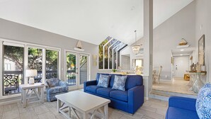 Ein geräumiges Wohnzimmer mit einem blauen Sofa, einem weißen Couchtisch und großen Fenstern.
