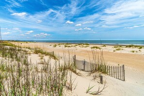 A sandy beach with a wooden fence and sparse vegetation.