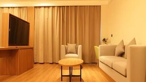 A modern living room with a wooden floor, a round table, a sofa, and a TV on a wooden stand. - Greentree Inn Lanzhou Zhongchuan Airport (Lanzhou)