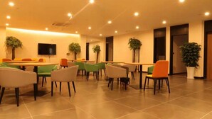 Un grand espace intérieur aménagé avec plusieurs tables et chaises, un téléviseur à écran plat fixé au mur et plusieurs plantes en pot.