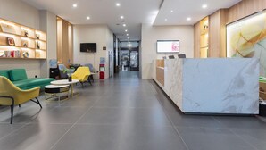 Un hall d’hôtel comprenant un comptoir d’accueil, un espace détente avec des canapés et des fauteuils, un téléviseur fixé au mur et une vitrine où sont exposés des trophées.