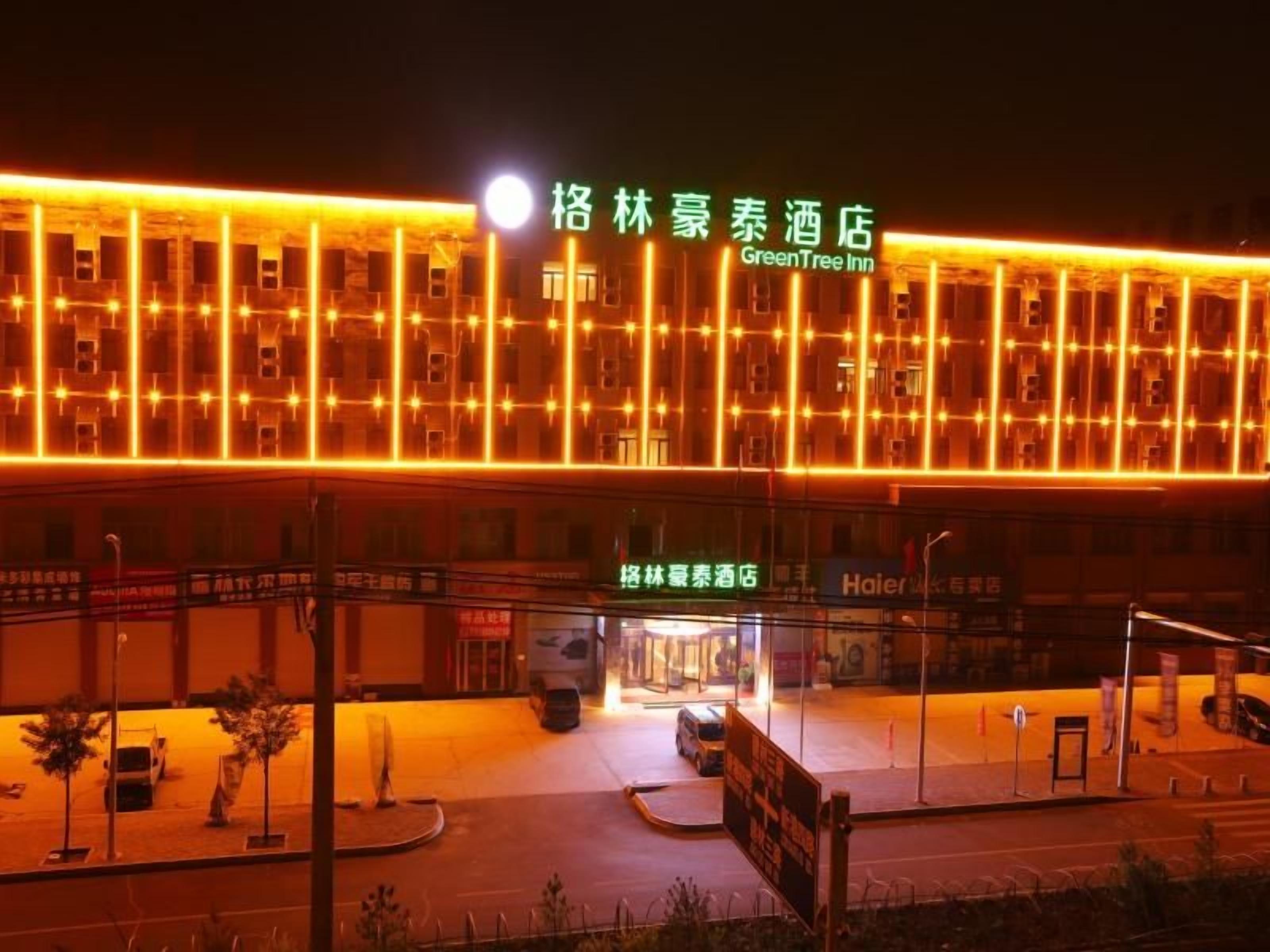 A hotel with a prominent illuminated facade at night, a clear entrance, and a visible parking area.