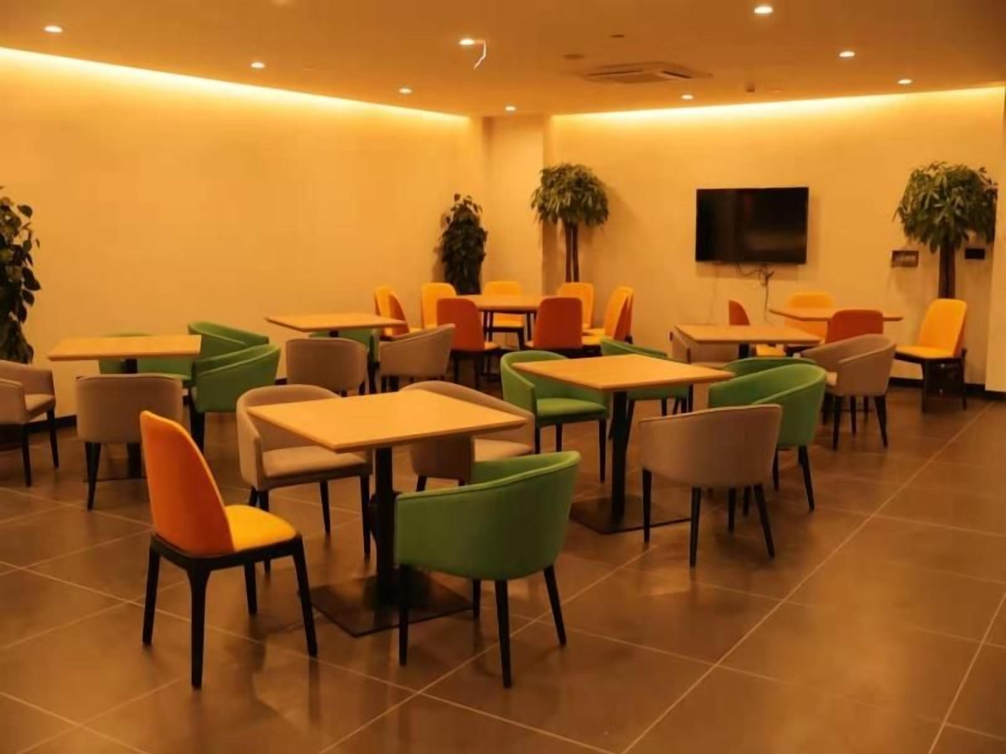 A dining area with multiple tables and chairs, a flat-screen TV mounted on the wall, and potted plants.