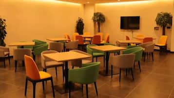 A dining area with multiple tables and chairs, a flat-screen TV mounted on the wall, and potted plants.