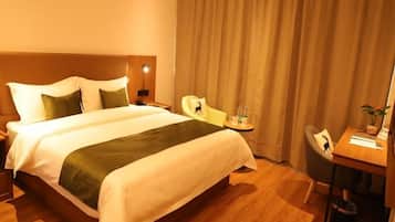 A hotel room with a large bed, a desk, a chair, and a curtain.