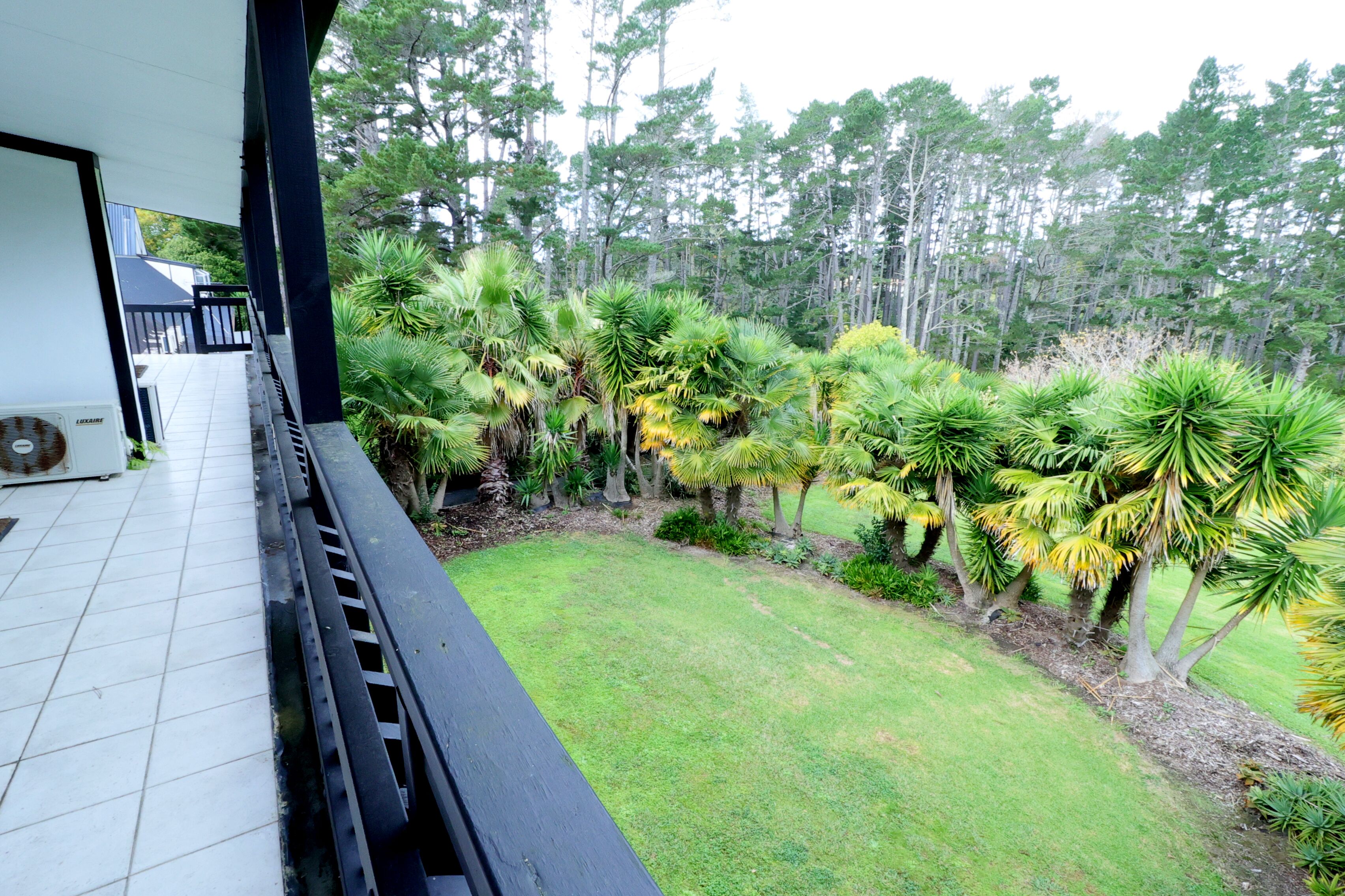 A balcony with a view of a well-maintained lawn and a variety of tropical plants.