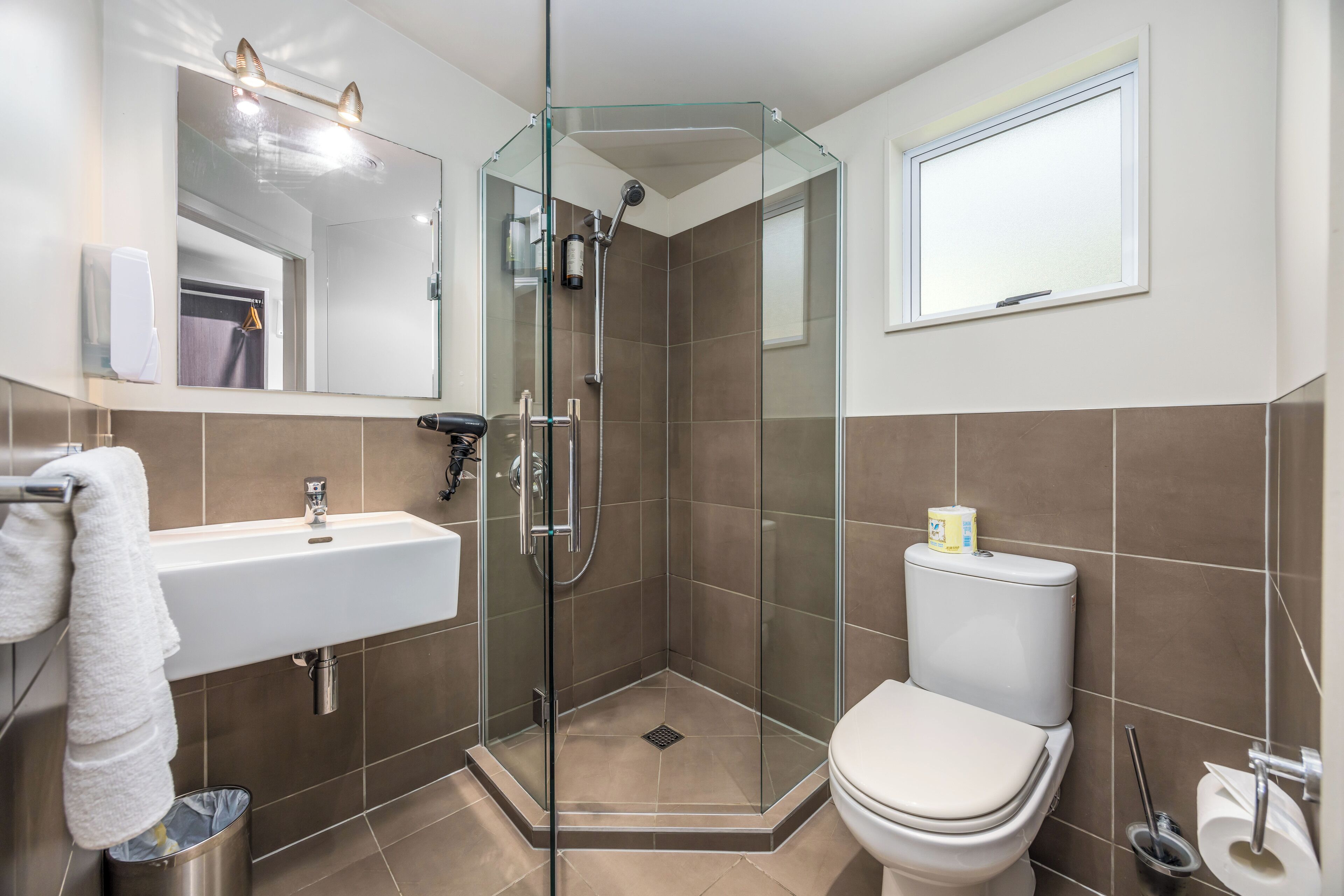 Un baño moderno con ducha de vidrio, un lavamanos blanco y un inodoro.