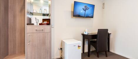 Een compacte hotelkamer met kitchenette, een kleine koelkast, een bureau met stoel, een flatscreen-tv aan de muur en een houten kledingkast.