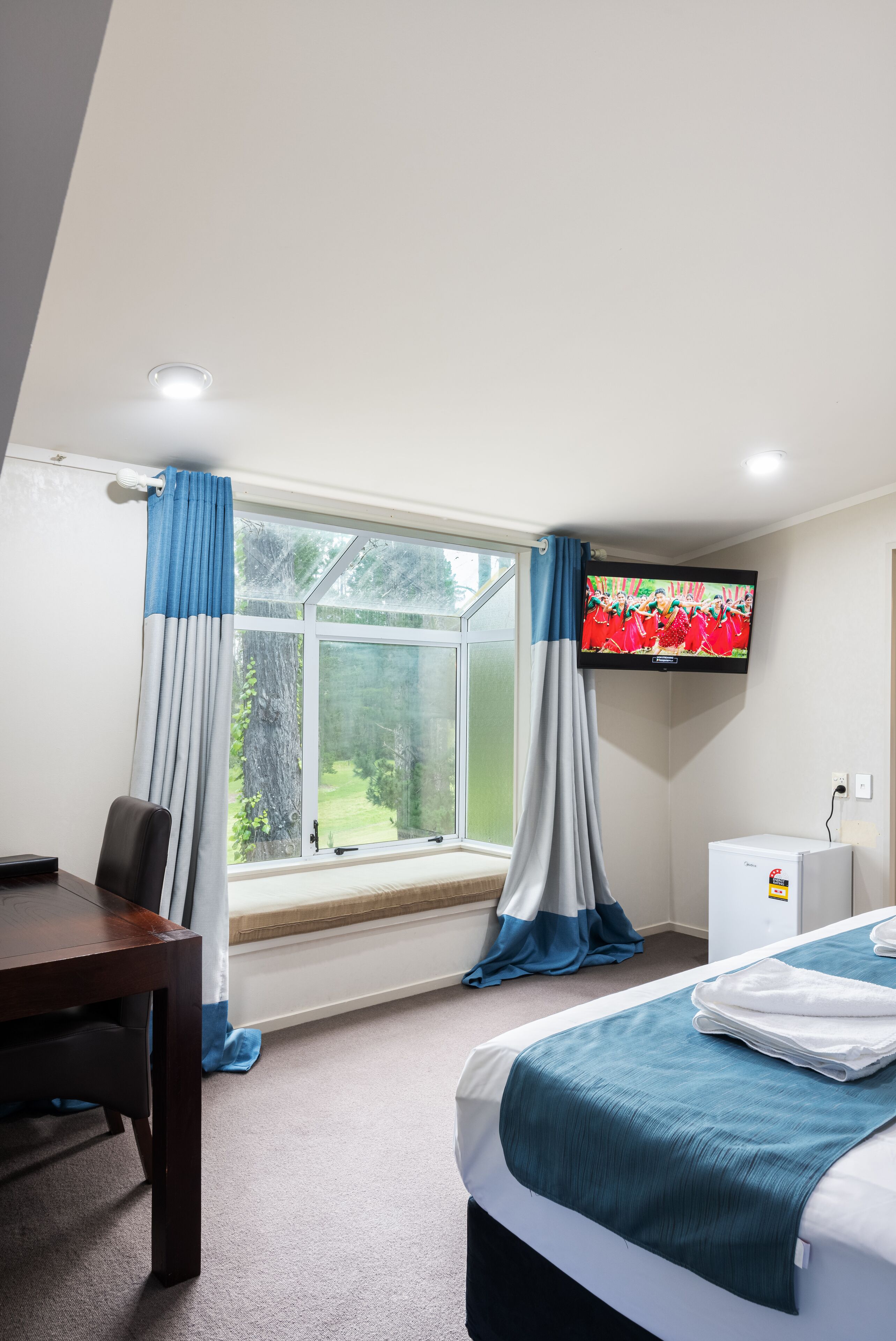 Habitació d'hotel amb un llit, una taula de treball, televisió i una finestra amb cortines.