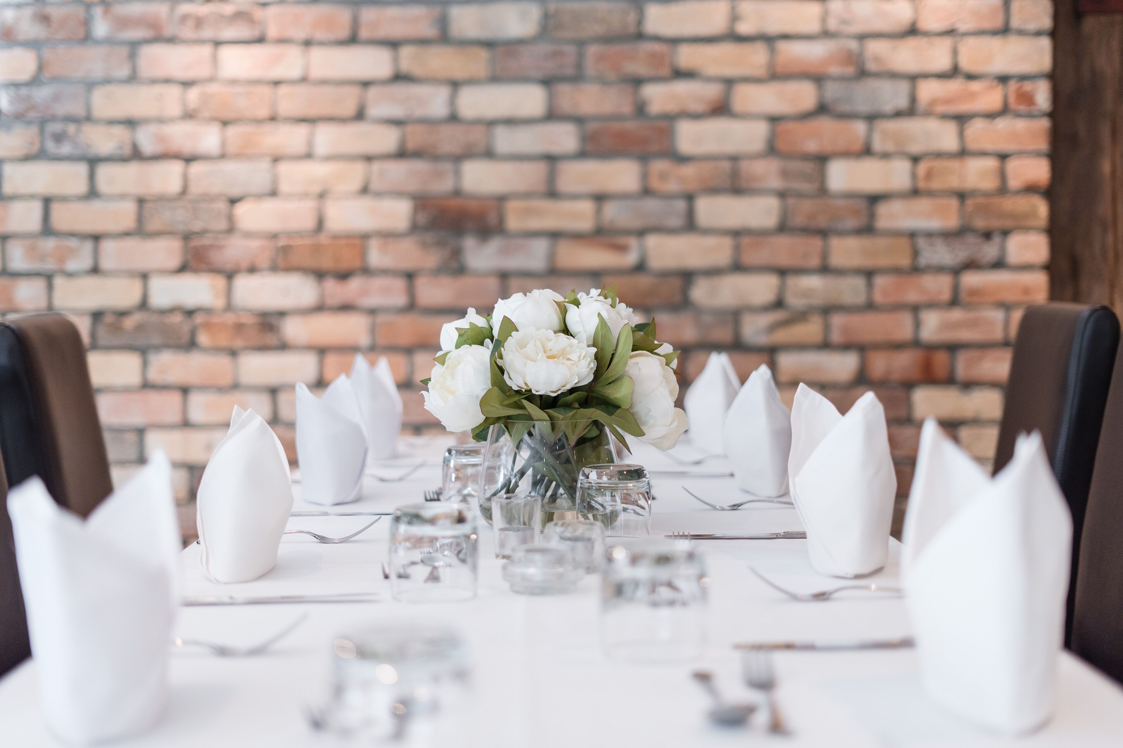 A dining table set with white napkins, clear glassware, and a centerpiece of white flowers.