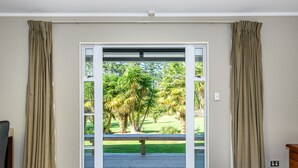 Een slaapkamer met een grote schuifdeur die leidt naar een balkon met uitzicht op palmbomen en een gazon.