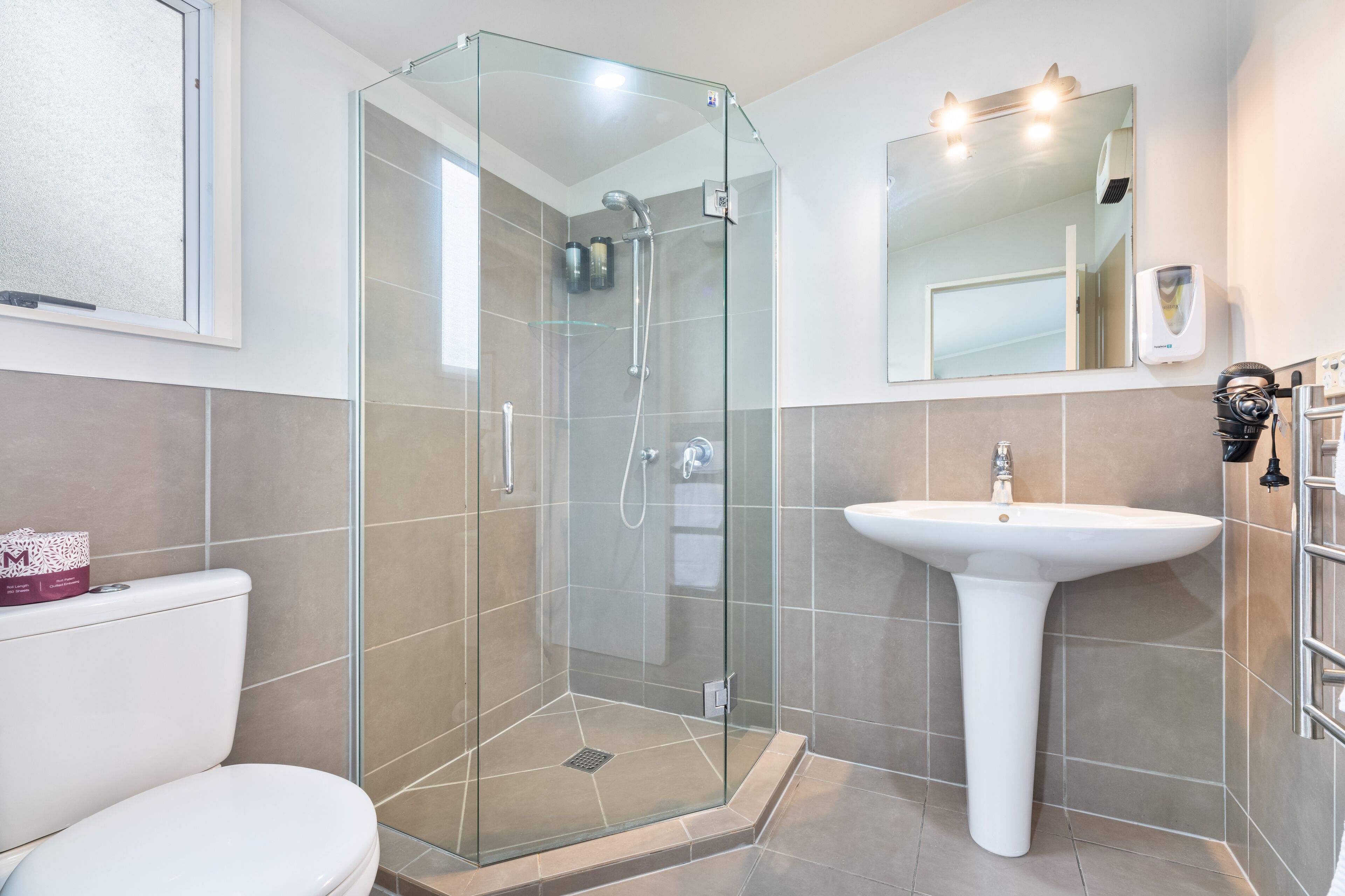 Un baño moderno con ducha de vidrio, lavamanos blanco y retrete.