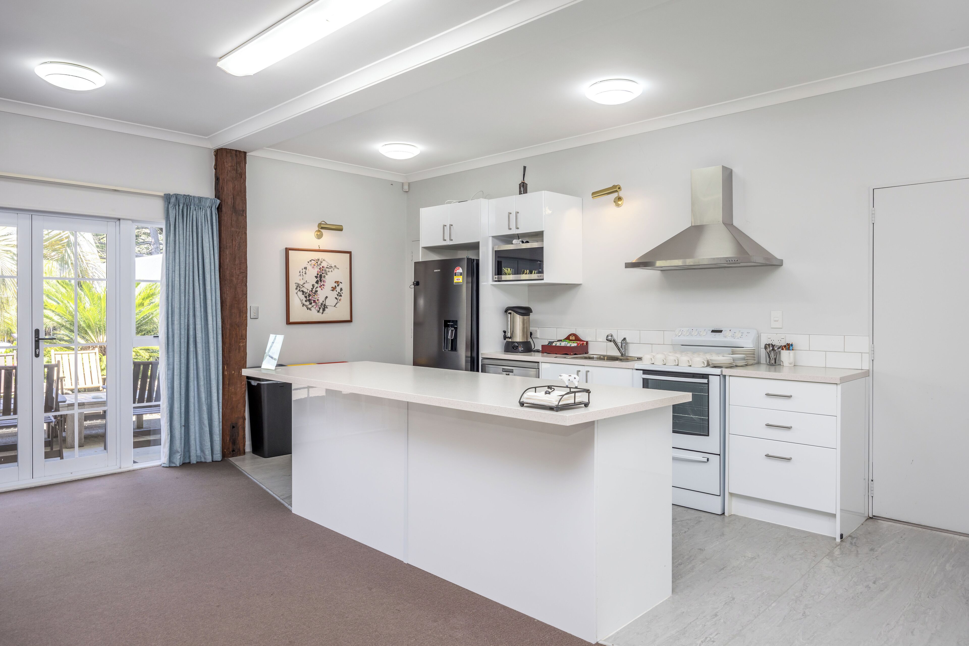 A modern kitchen with white cabinetry, a central island, and a stainless steel range hood.