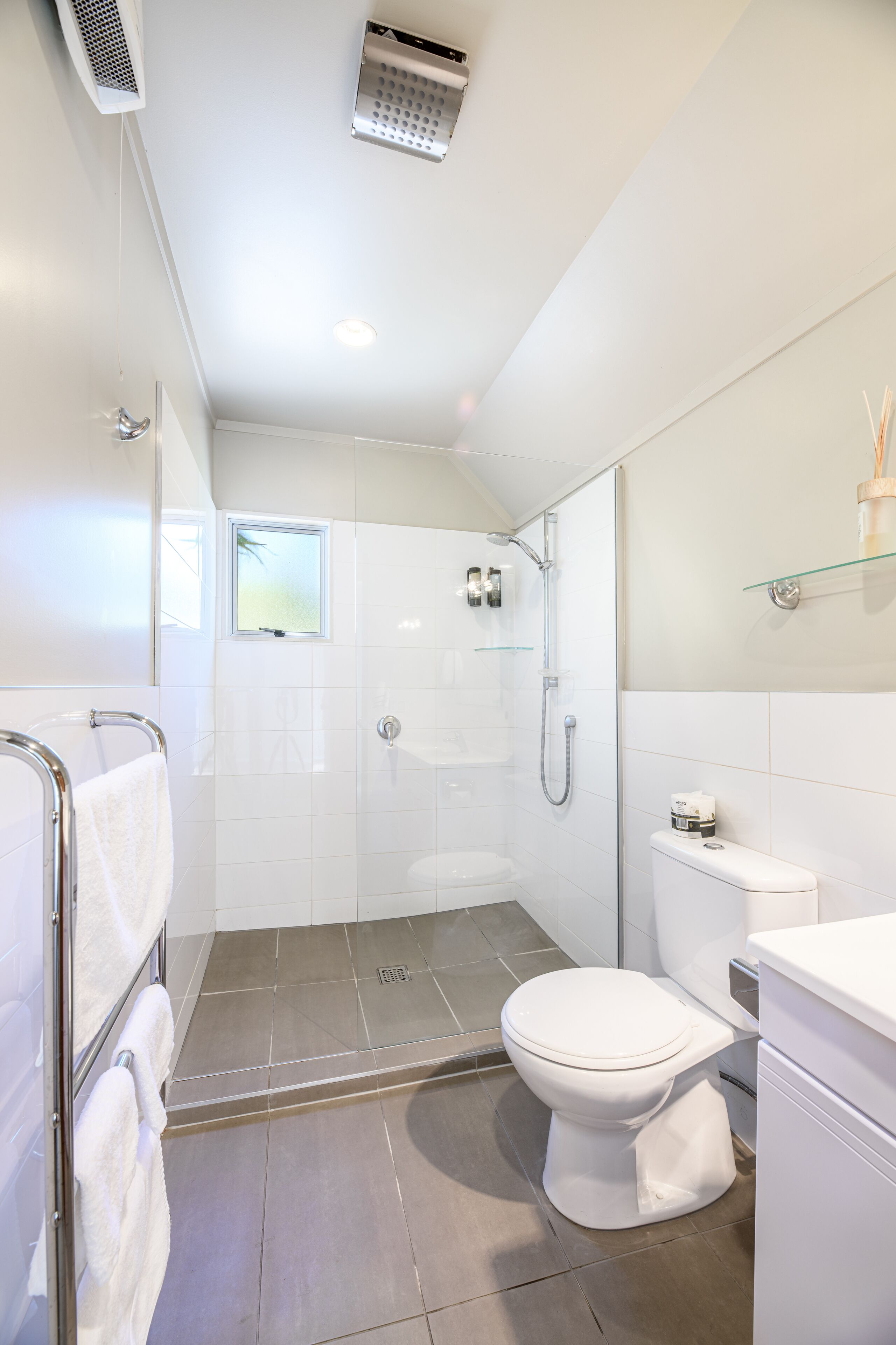 A modern bathroom with a glass shower enclosure, a toilet, and a glass shelf above the sink.