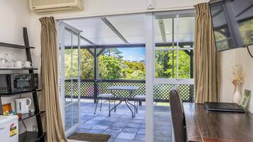 Una stanza con una porta vetrata scorrevole che dà su un balcone con tavolo e sedie, un forno a microonde, una macchina da caffè e un piccolo frigorifero.