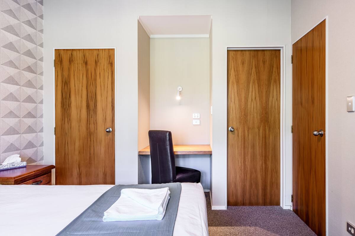 A hotel room with a bed, a desk, and two wooden doors.