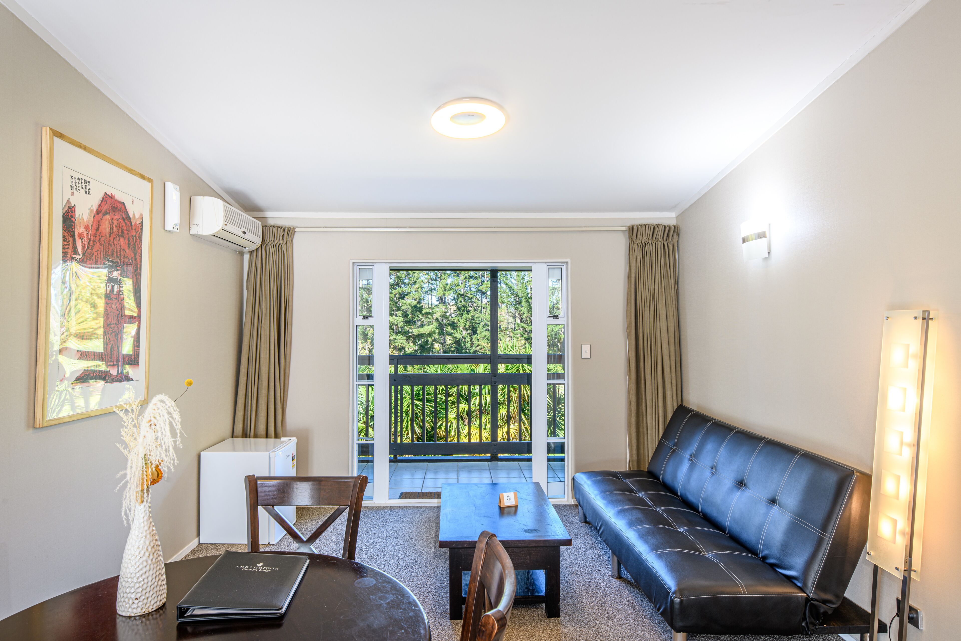 A room with a sofa, a table, a chair, a small decorative vase, a framed picture, and a window with curtains.