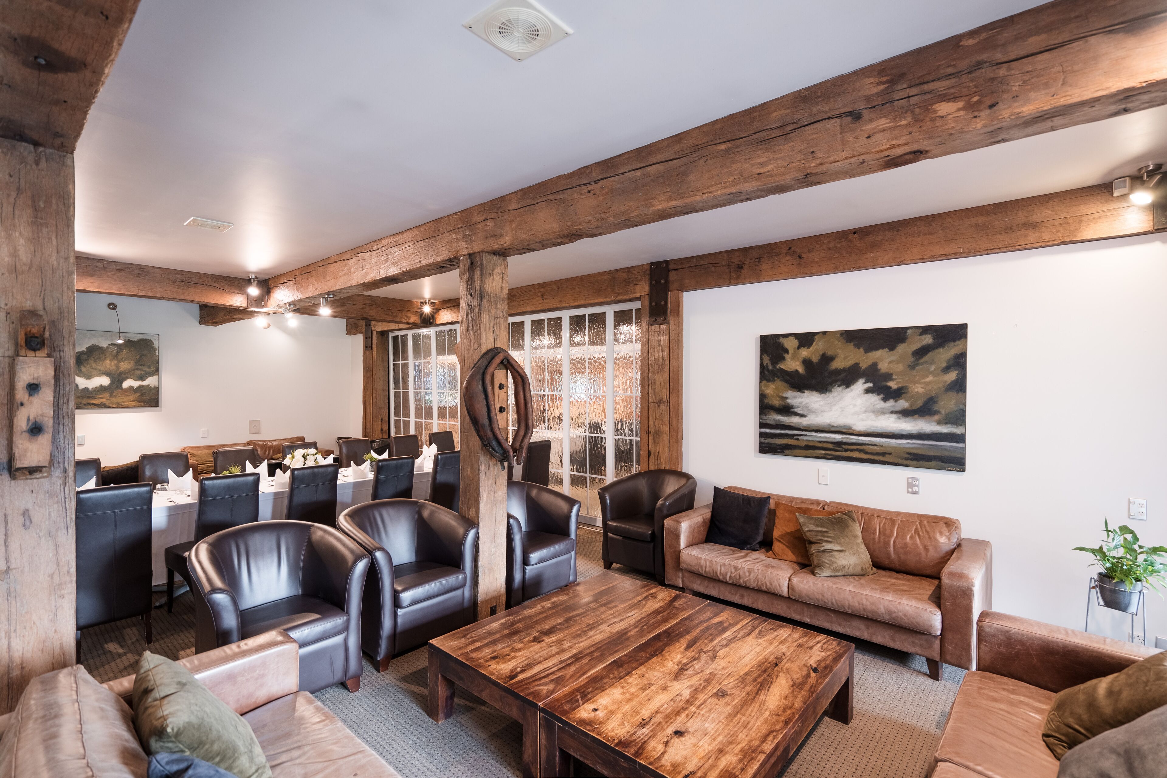 A spacious room with a wooden ceiling, leather chairs, a wooden coffee table, and a sofa.