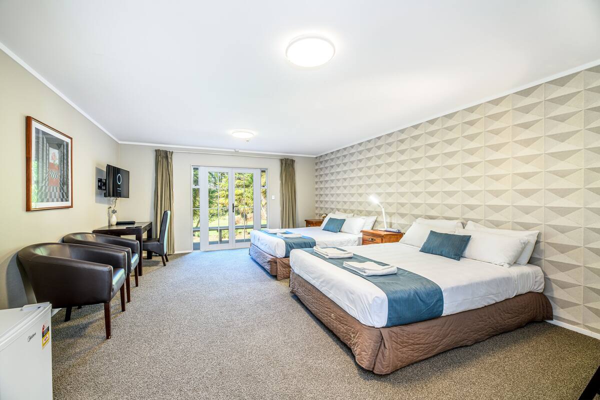 A hotel room with two beds, a desk, and a chair. There is a television on the wall and a window with curtains.