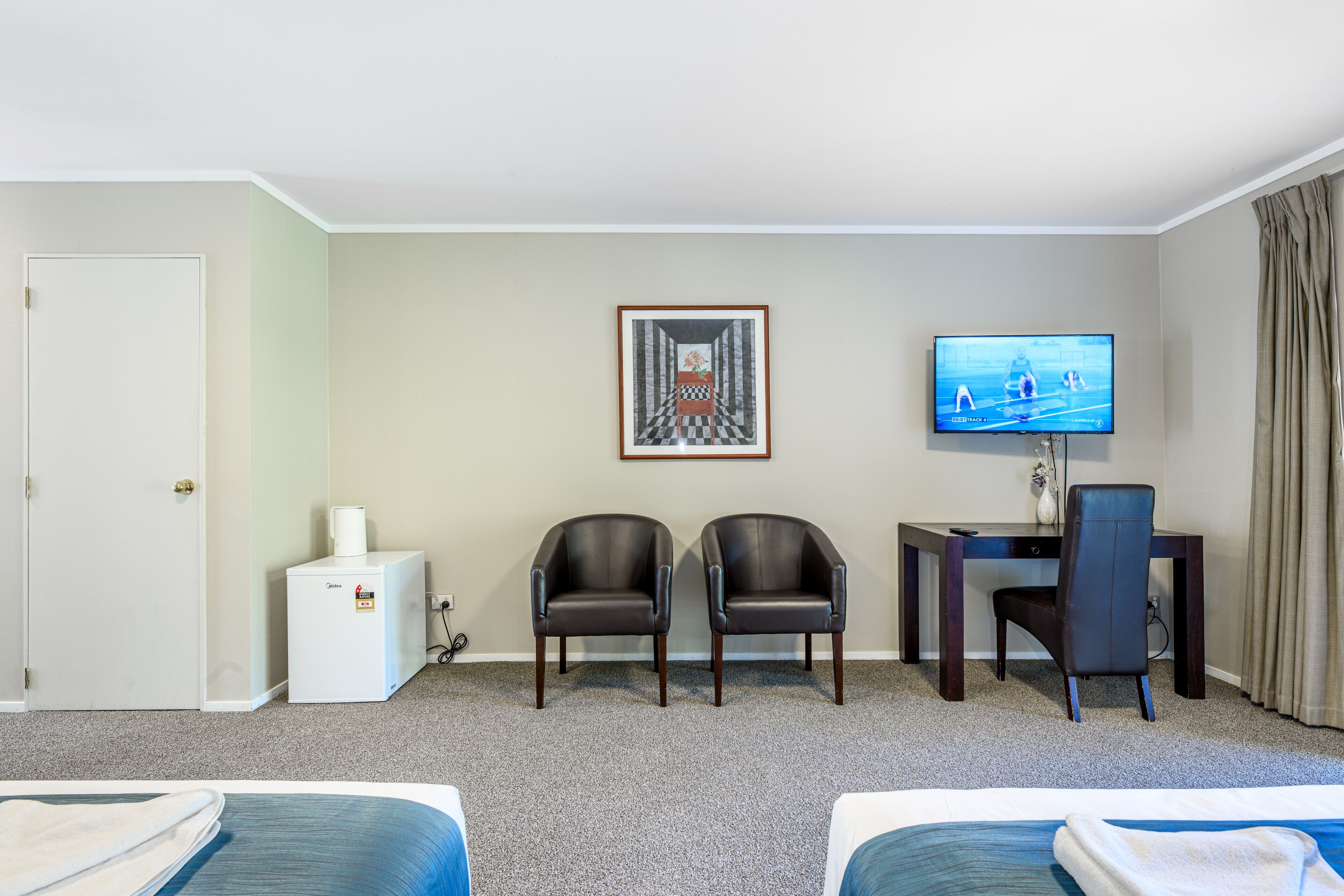 Habitación de hotel con dos camas, un escritorio con silla, un televisor y un cuadro en la pared.