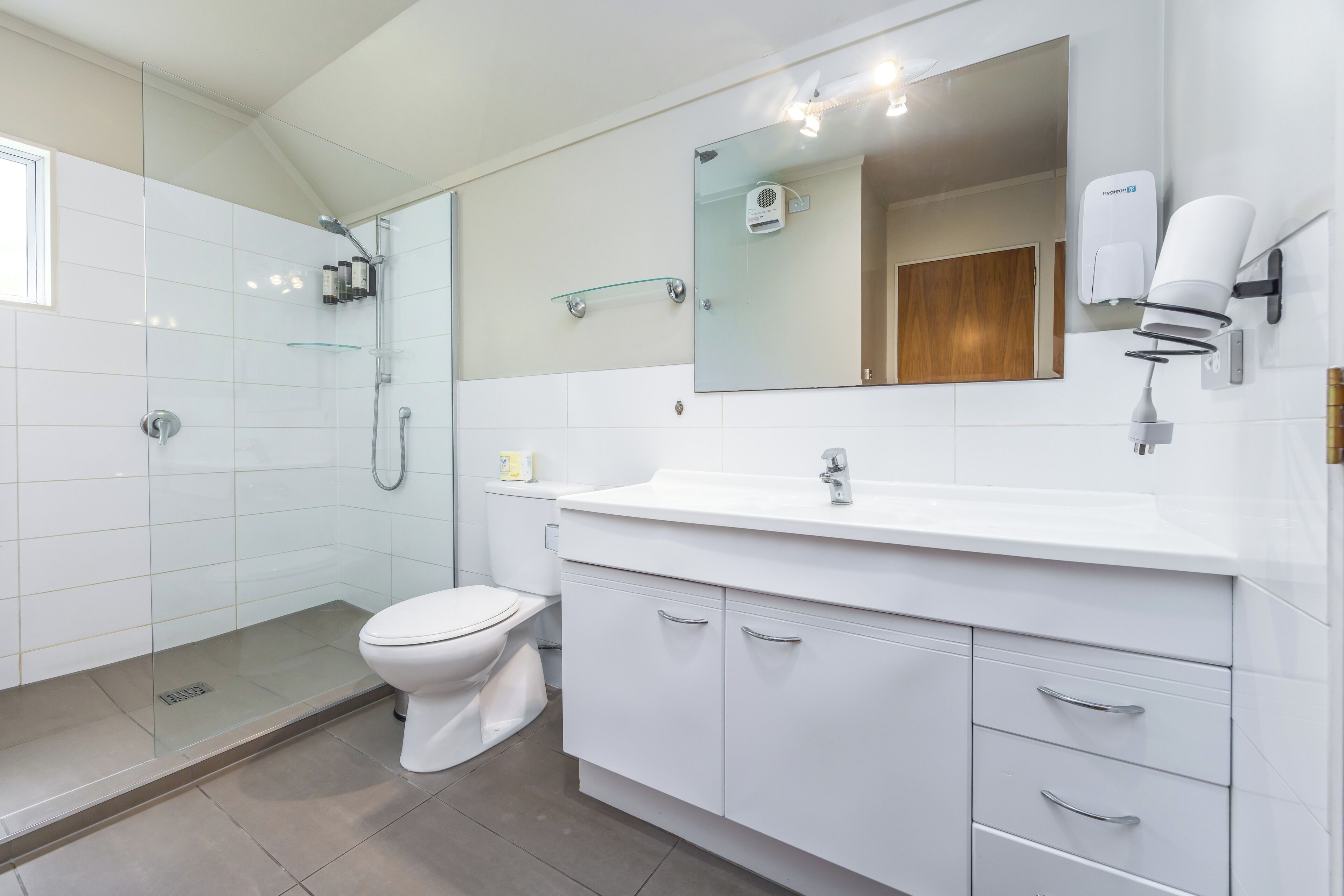A modern bathroom with a glass shower enclosure, a white toilet, a large mirror, and a white sink with a vanity.