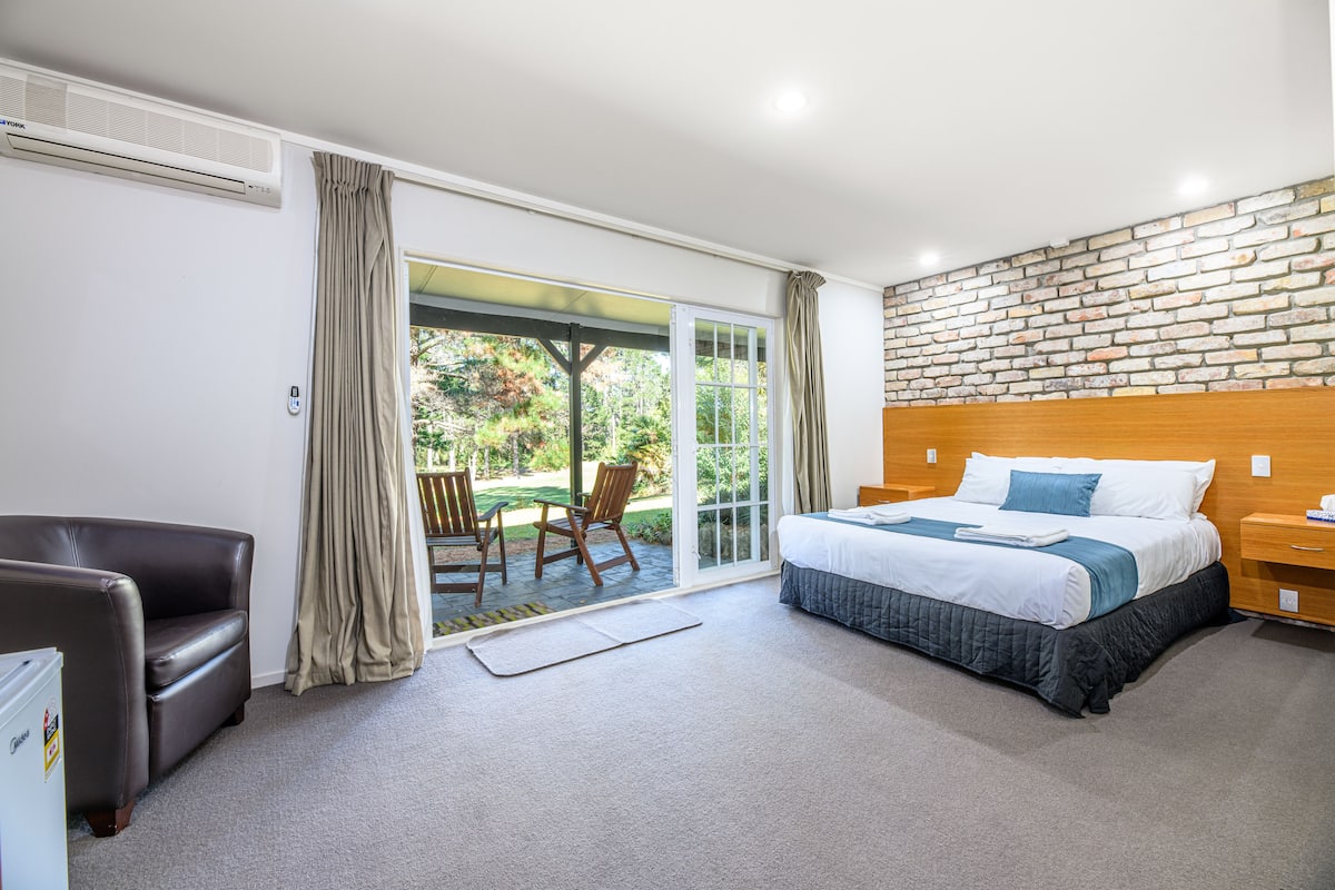 A hotel room with a bed, a desk, a chair, and a sliding glass door leading to an outdoor area.