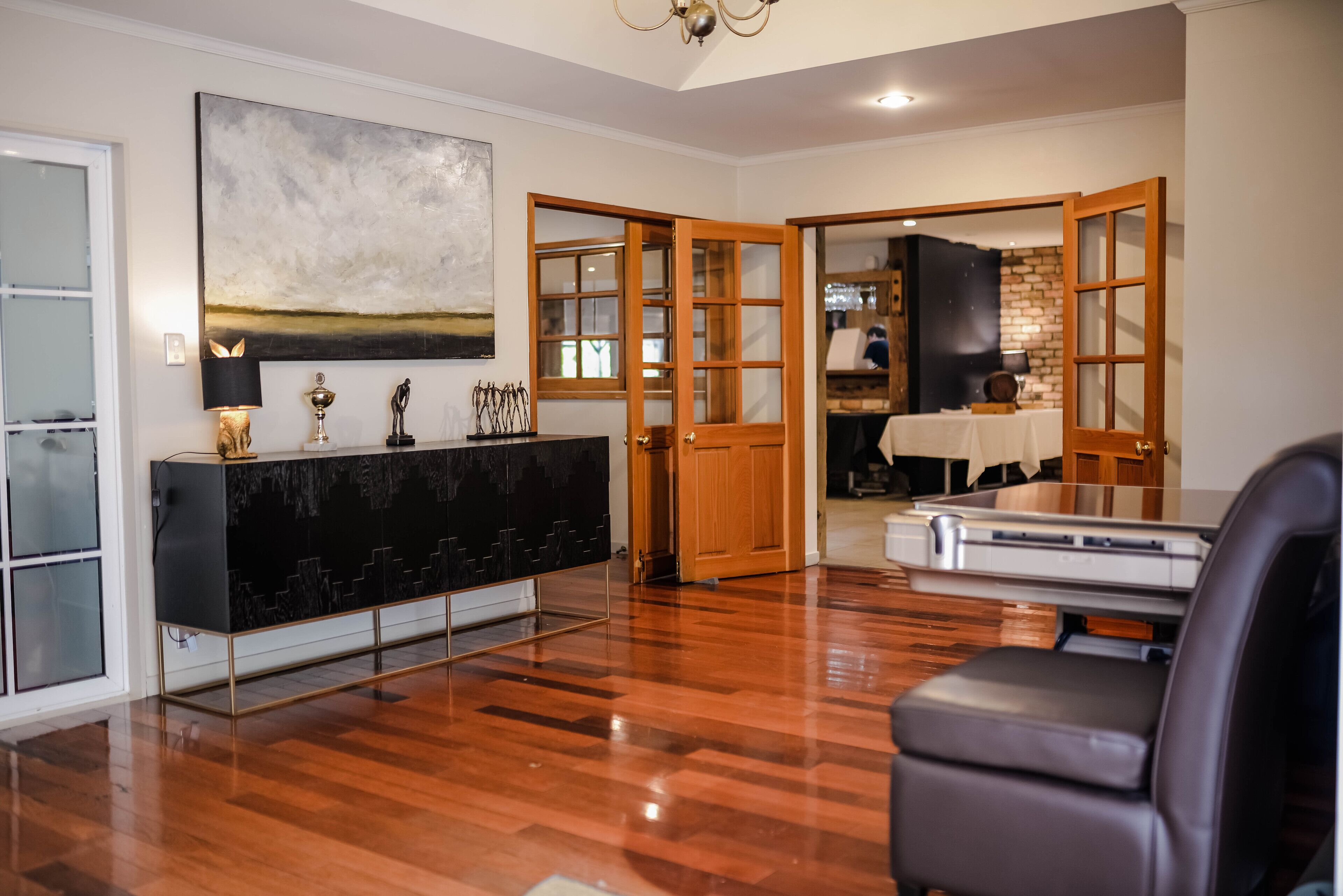 A spacious living room with a wooden floor, a black entertainment unit, and a large abstract painting on the wall.