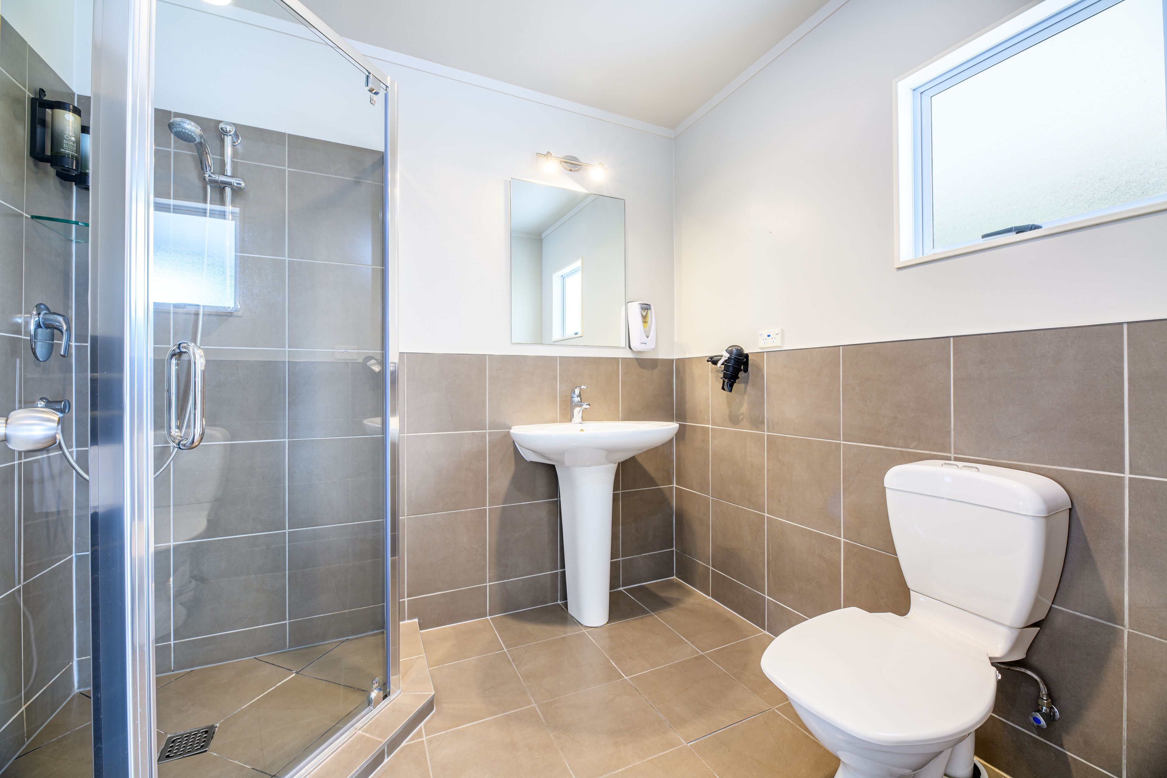 A modern bathroom with a glass-enclosed shower, a white pedestal sink, and a toilet.