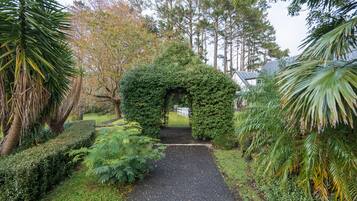 A pathway leading through a garden with a central archway surrounded by various plants and trees.