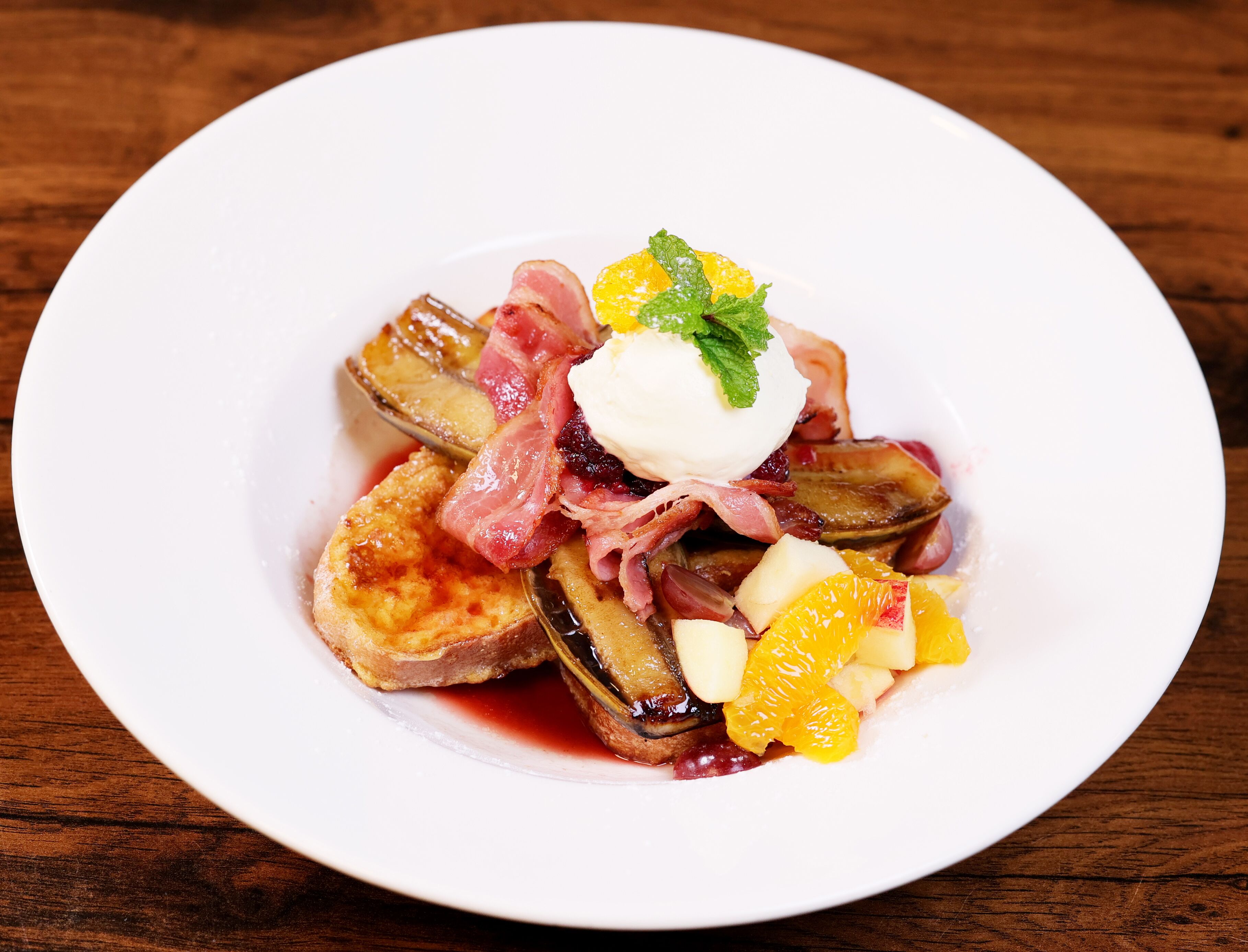 Ein weißer Teller mit Dessert, bestehend aus Früchten, möglicherweise Orangenscheiben und einem pochierten Ei, auf einem Holztisch.