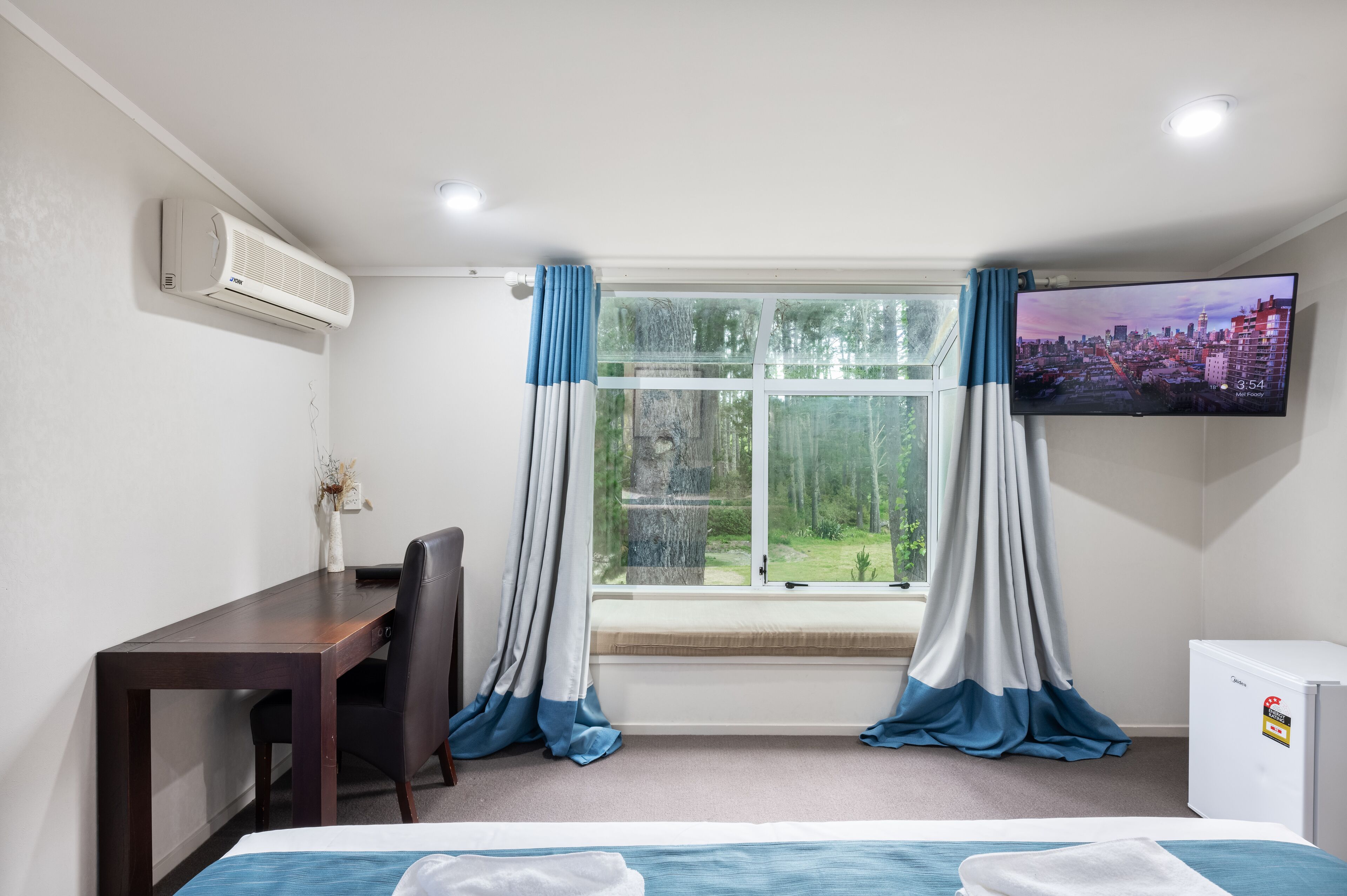 Una camera d'albergo con un letto, una scrivania, una sedia, un televisore e una finestra con tende.