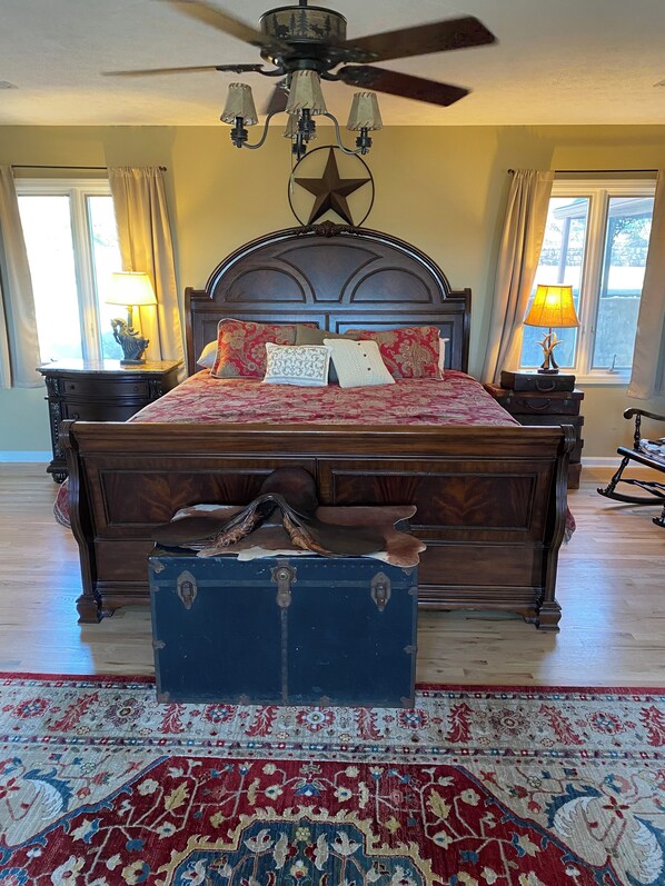 A bedroom with a large bed, a ceiling fan, a star-shaped wall decoration, and a vintage suitcase in front of the bed.