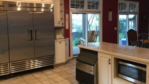 Une cuisine avec des meubles blancs, un réfrigérateur en acier inoxydable, un four à micro-ondes et une poubelle.