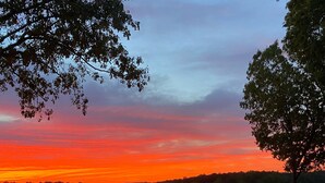 Une vue sur un coucher de soleil au-dessus d’un lac, avec une clôture et des arbres au premier plan.