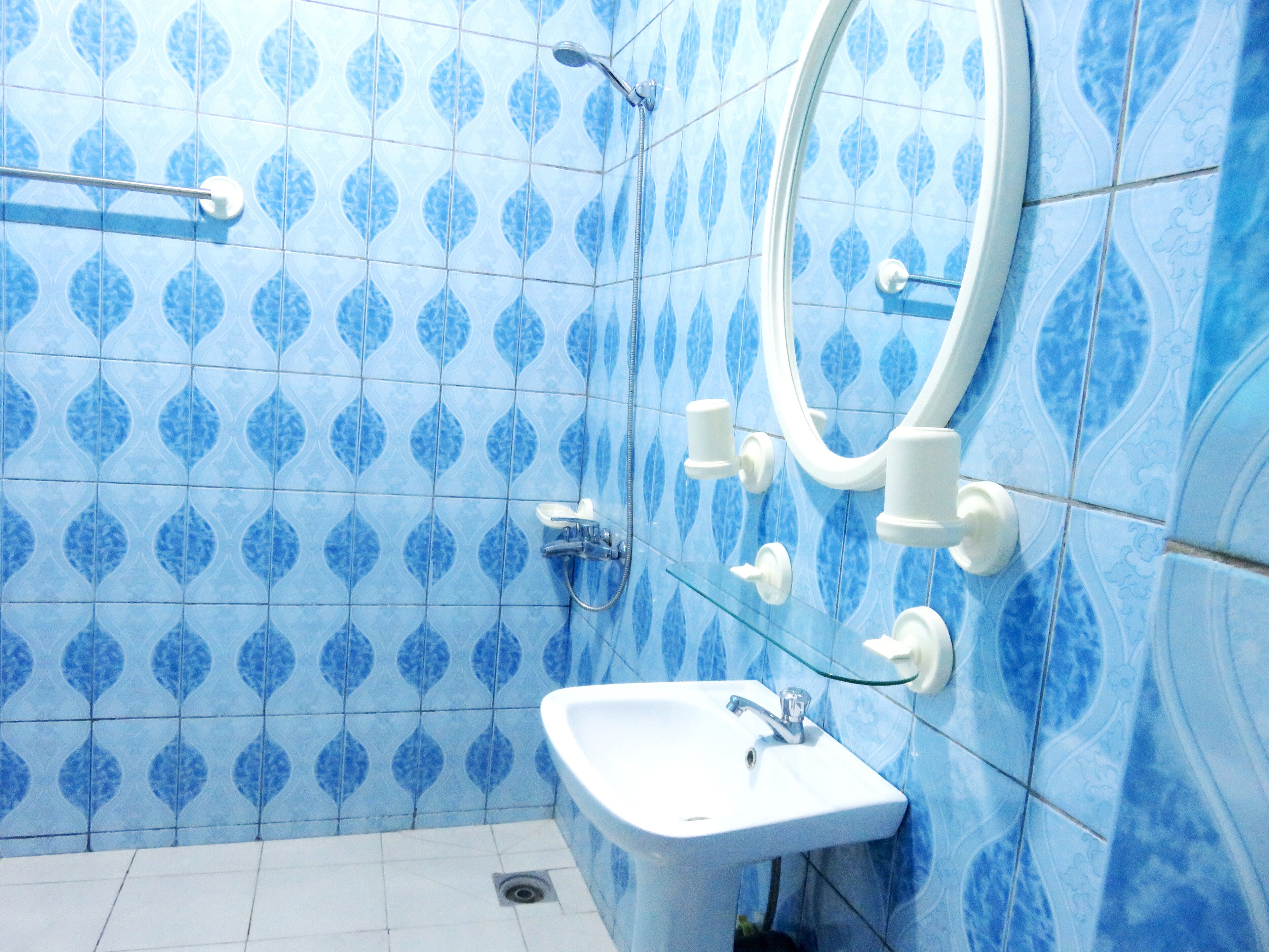 Un baño con azulejos azules estampados, un lavabo blanco y un espejo.