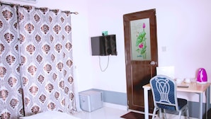 A room with a bed, a desk with a chair, a television, and a door with a floral design. - Nora Hotel (Cotonou)