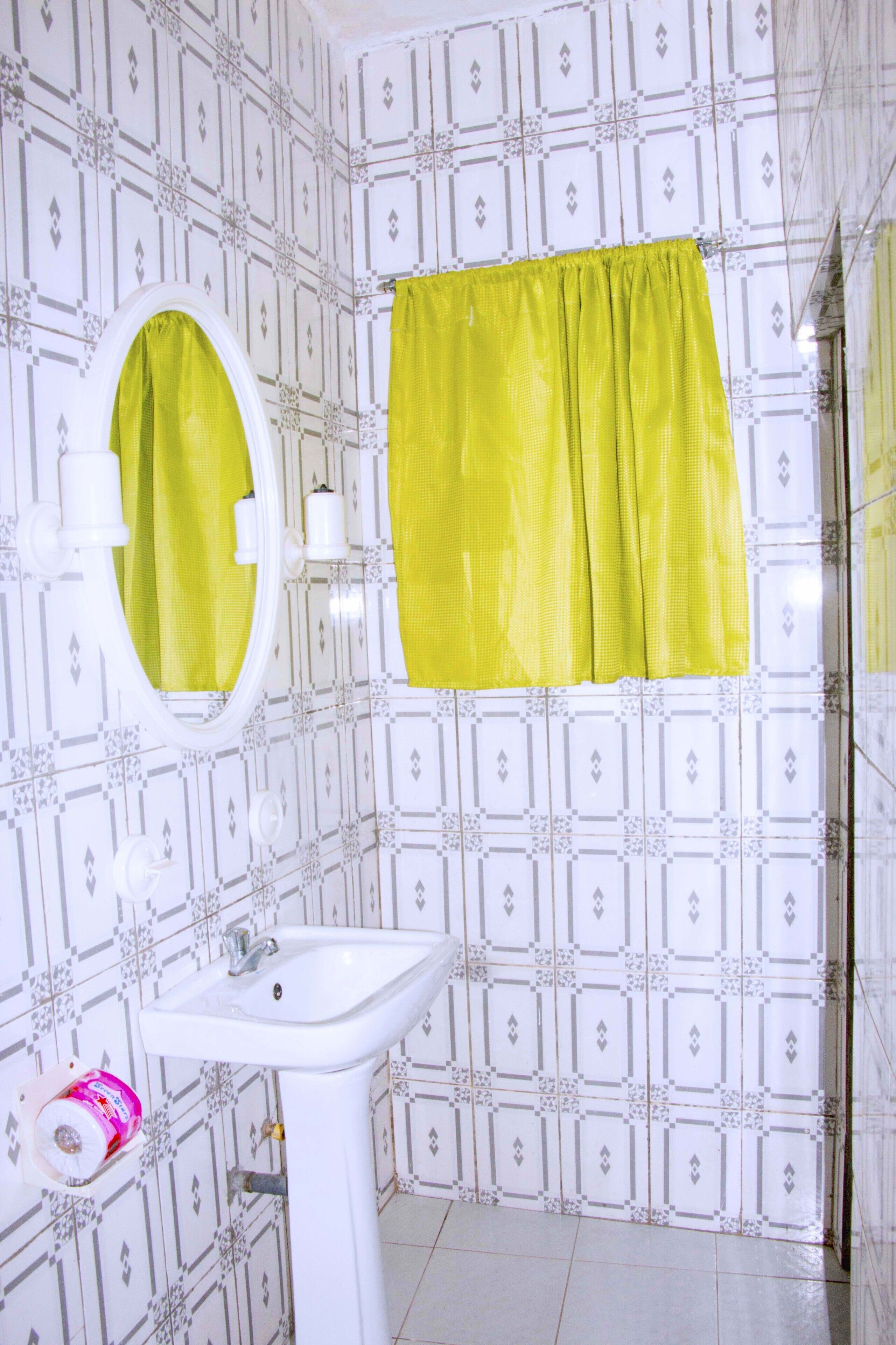 Une salle de bain avec un lavabo blanc, un miroir et un rideau de douche jaune.