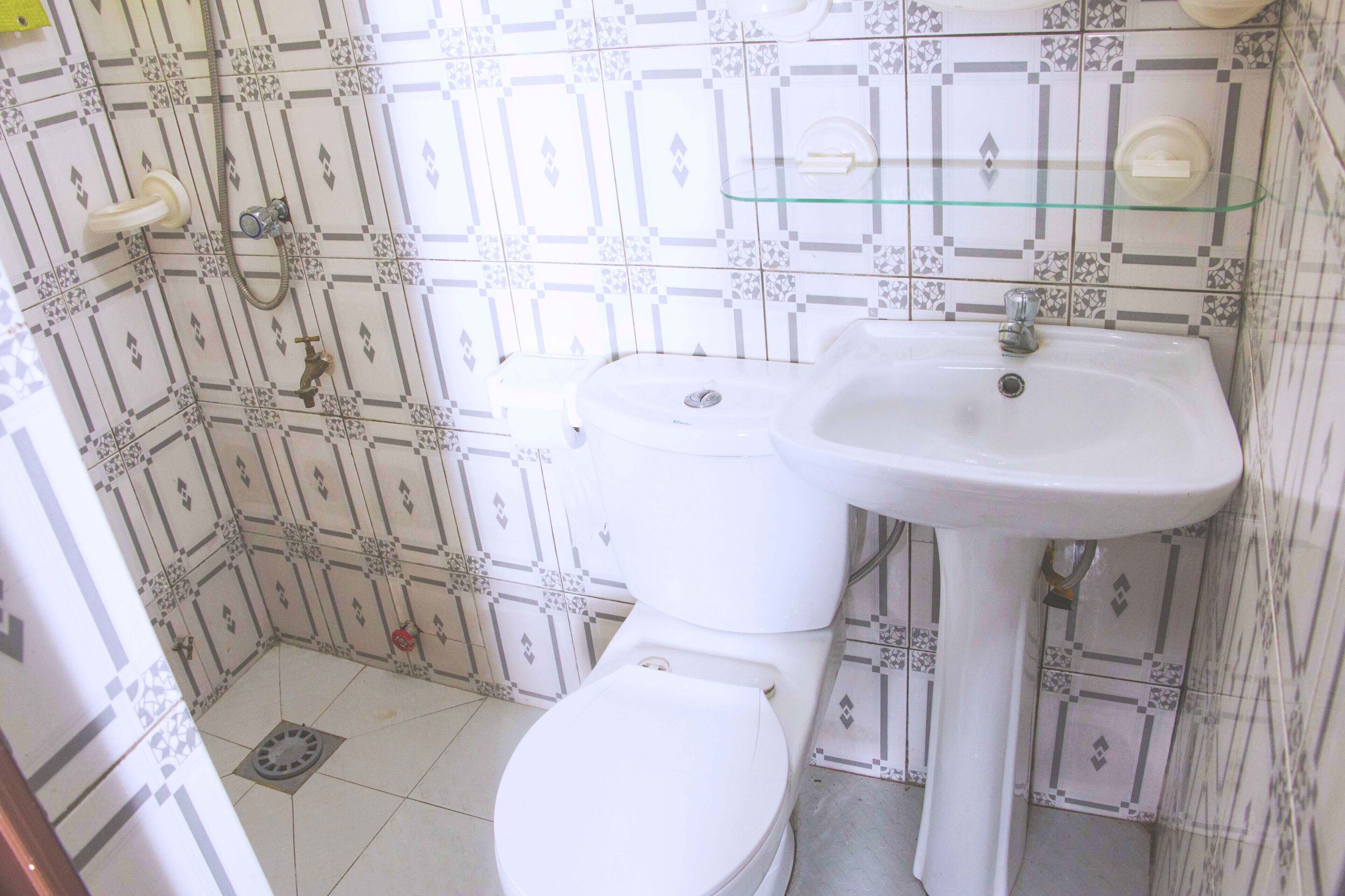 Une salle de bain comprenant des toilettes, un lavabo et une douche. Les murs sont recouverts de carreaux décoratifs.