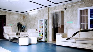 A spacious living area with a white sofa, a white armchair, and a glass coffee table. A minibar is visible in the corner. - Nora Hotel (Cotonou)