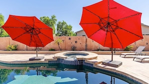 A swimming pool with two red umbrellas, lounge chairs, and a decorative wall with plants. - Westgate Wonder ~ A Resort-Style Oasis w/ Heated Pool, Spa, Game Rooms, Putting Green & More! (Glendale)