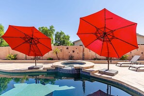 Piscina com dois guarda-sóis vermelhos, espreguiçadeiras e um muro decorativo com plantas.