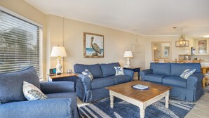 Ein Wohnzimmer mit zwei blauen Sofas, einem Couchtisch und einem Vogelbild an der Wand.