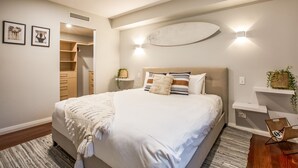 A bedroom with a large bed, bedside tables, a built-in wardrobe, and a wall-mounted shelf with plants.