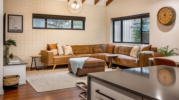 A modern living room with a sectional sofa, a dining area, and a large window providing natural light.