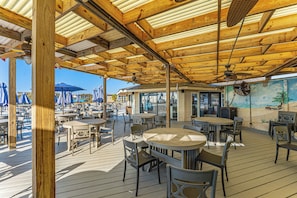 Un espace extérieur aménagé avec des tables et des chaises en bois, un ventilateur de plafond et une fresque murale.